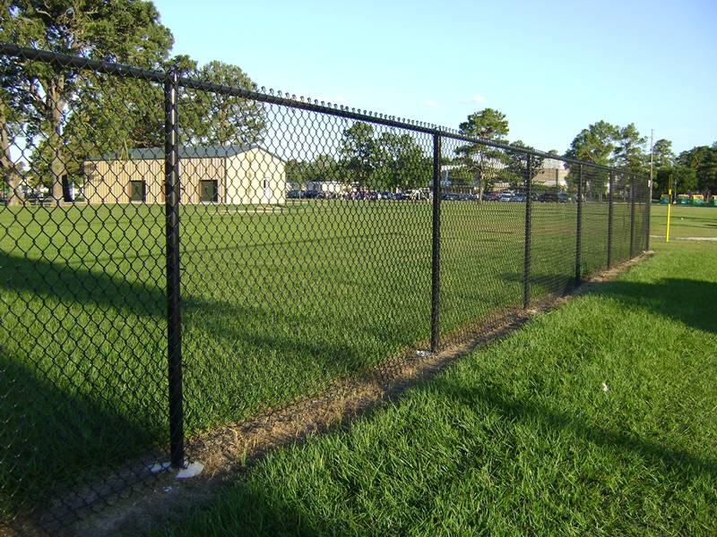 Chain link fence installed on the border of far wheat field in residential area distance
