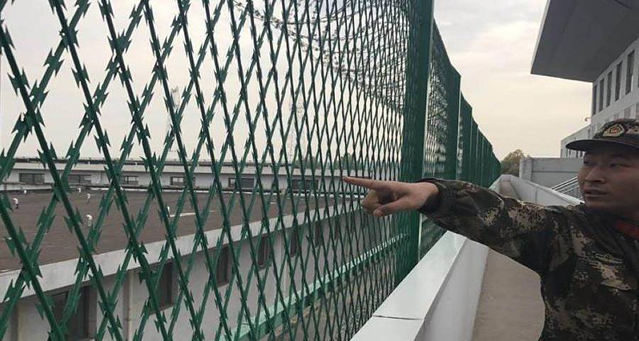 A patrolling soldier points his finger at the welded razor mesh prison fence
