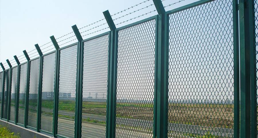 Expanded metal fence with barbed wire on top installed on the side of the road