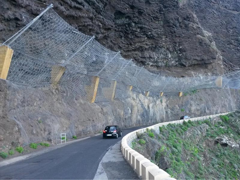 A rockfall barrier installed on a hillside on one side of the road.